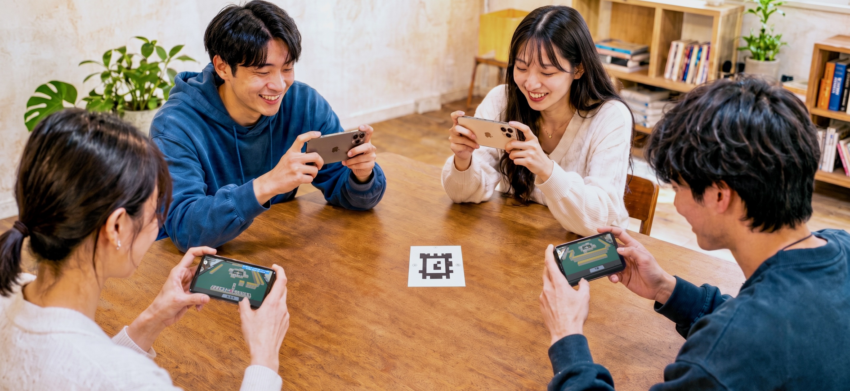 机を囲んだ4人が、中央に置いたマーカーシートへそれぞれのiPhoneを向けて対局している様子
